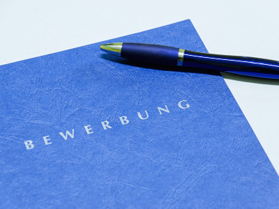 Blaue Bewerbungsmappe mit einem danebenliegenden Kugelschreiber.