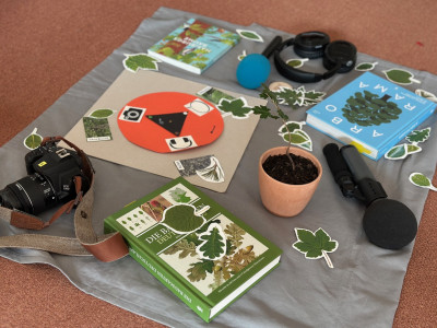 auf einer Decke liegen eine Kamera, Mikrofone, Kopfhörer, Baumbestimmungsbücher, Blätter, ein Baum im Umtopf