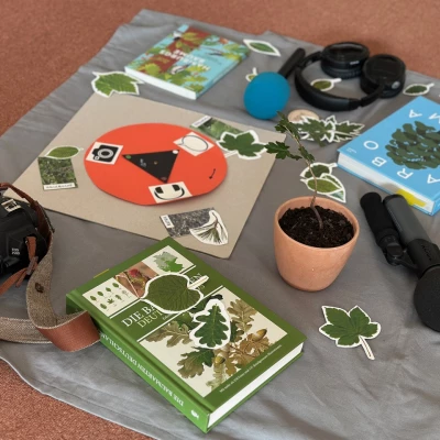 auf einer Decke liegen eine Kamera, Mikrofone, Kopfhörer, Baumbestimmungsbücher, Blätter, ein Baum im Umtopf