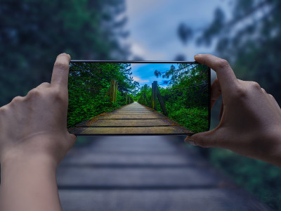 Zwei Hände halten ein Smartphone. Auf dem Screen ist eine Brücke mit Büschen an den Seiten sichtbar.
