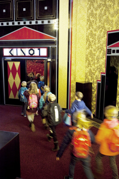 SchulKinoWoche Hamburg. Einlass im Passage Kino. Zu sehen ist die Tür von Saal 1 und eine Gruppe von Kindern von hinten, die den Saal betreten.