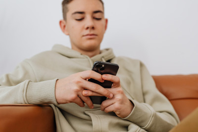 Junge sitzt auf einem Sofa und schaut auf ein Smartphone