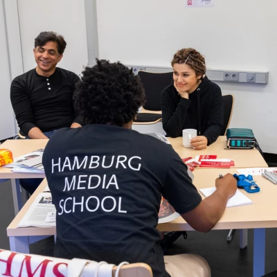 Fotos von vier Personen, die bei einem Tag der Offenen Tür der Hamburg Media School vor Ort waren. Eine Person ist in der Rückenansicht zu sehen und trägt ein dunkelblaues T-Shirt mit dem Aufdruck 