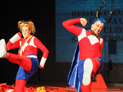 Zwei Darstellende aus dem Theaterstück Friend Simulator in rot-blauen Kostümen auf der Bühne.