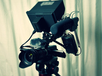 Videokamera auf Stativ mit angebrachtem Mikrofon.