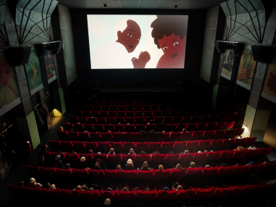 Blick in einen Kinosaal des zeise Kinos mit Kindern auf den Sitzen. Auf der Leinwand sind zwei gezeichnete Filmfiguren zu sehen.